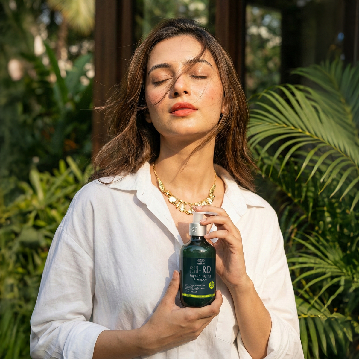 A woman in a white shirt holds a dark green bottle of ROF Organic Rosehip Seed Serum against a lush green tropical background.