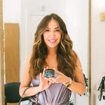 Woman holding a small electronic device in a room with wooden furniture.