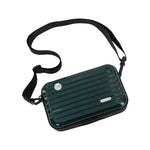 A dark green hard-shell crossbody bag with a black adjustable shoulder strap, featuring a ribbed texture and a small silver brand plaque.